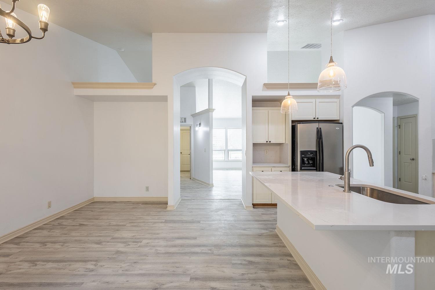4227 North Rhodes Avenue Meridian, ID 83646 - Photo 9 of 42 Kitchen featuring arched walkways, stainless steel fridge, a high ceiling, light wood-type flooring, and light stone counters