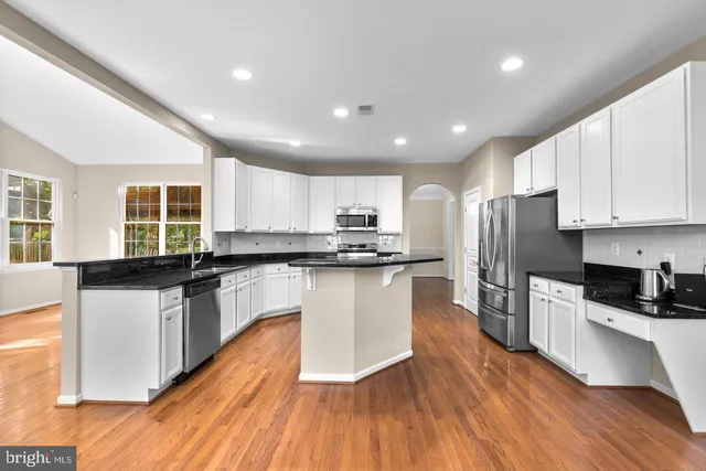 a kitchen with stainless steel appliances granite countertop a refrigerator a stove top oven a sink dishwasher and white cabinets with wooden floor