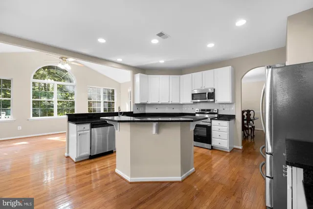 a kitchen with stainless steel appliances granite countertop a refrigerator a sink dishwasher a stove and white countertops with wooden floor