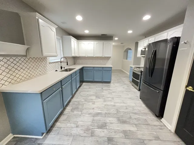 a large kitchen with a large counter top a refrigerator and cabinets