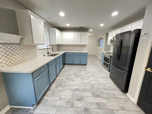 a large kitchen with a large counter top a refrigerator and cabinets