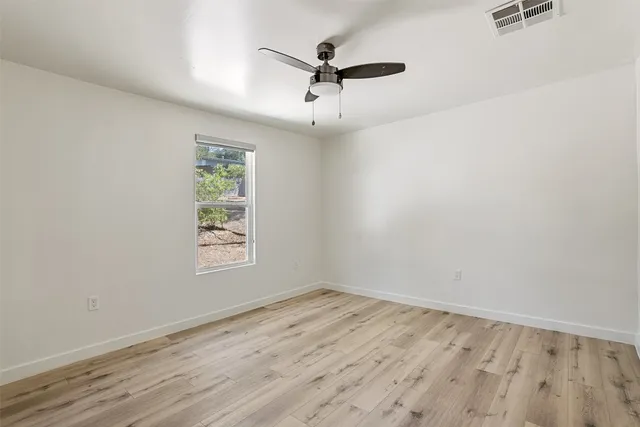an empty room with wooden floor ceiling fan and windows