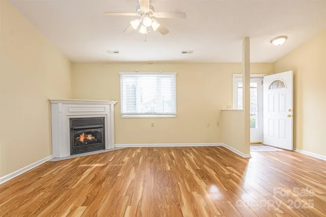 a view of an empty room with wooden floor fireplace and a window