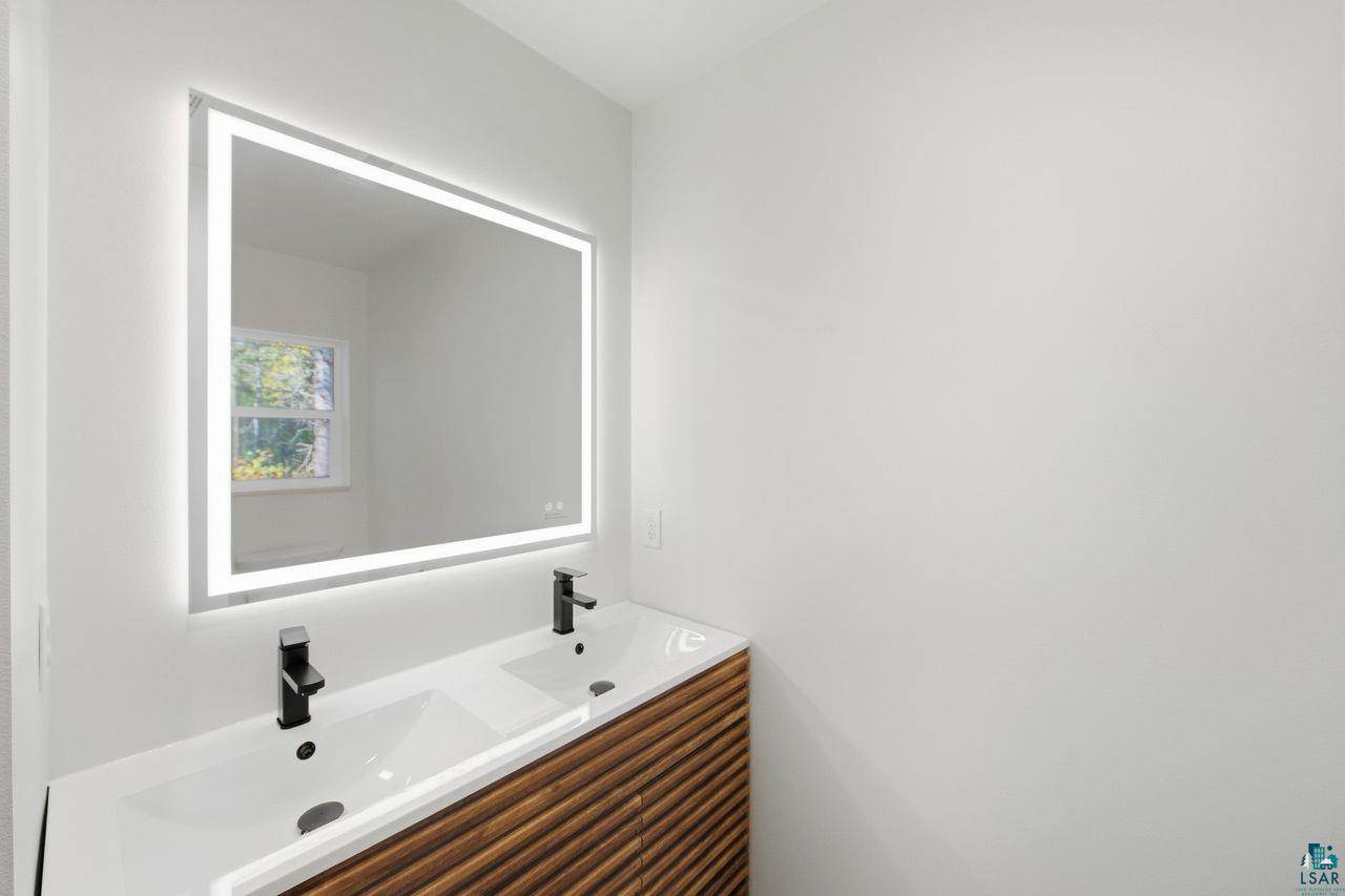 65352 Adler Road Marengo, WI 54855 - Photo 18 of 24 Illuminated vanity mirror, dual integrated sinks, matte black single-handle faucets, and a wood-finish vanity with horizontal slat detailing