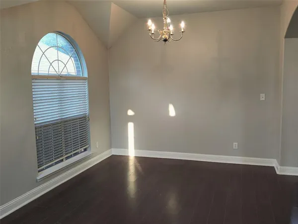 an empty room with wooden floor chandelier and windows