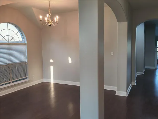 an empty room with wooden floor chandelier and windows