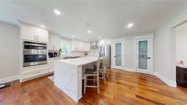 a kitchen with stainless steel appliances kitchen island granite countertop a stove top oven a sink dishwasher a refrigerator and white cabinets with wooden floor