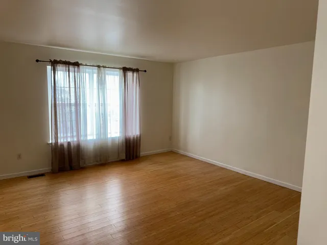 an empty room with wooden floor and windows with curtains