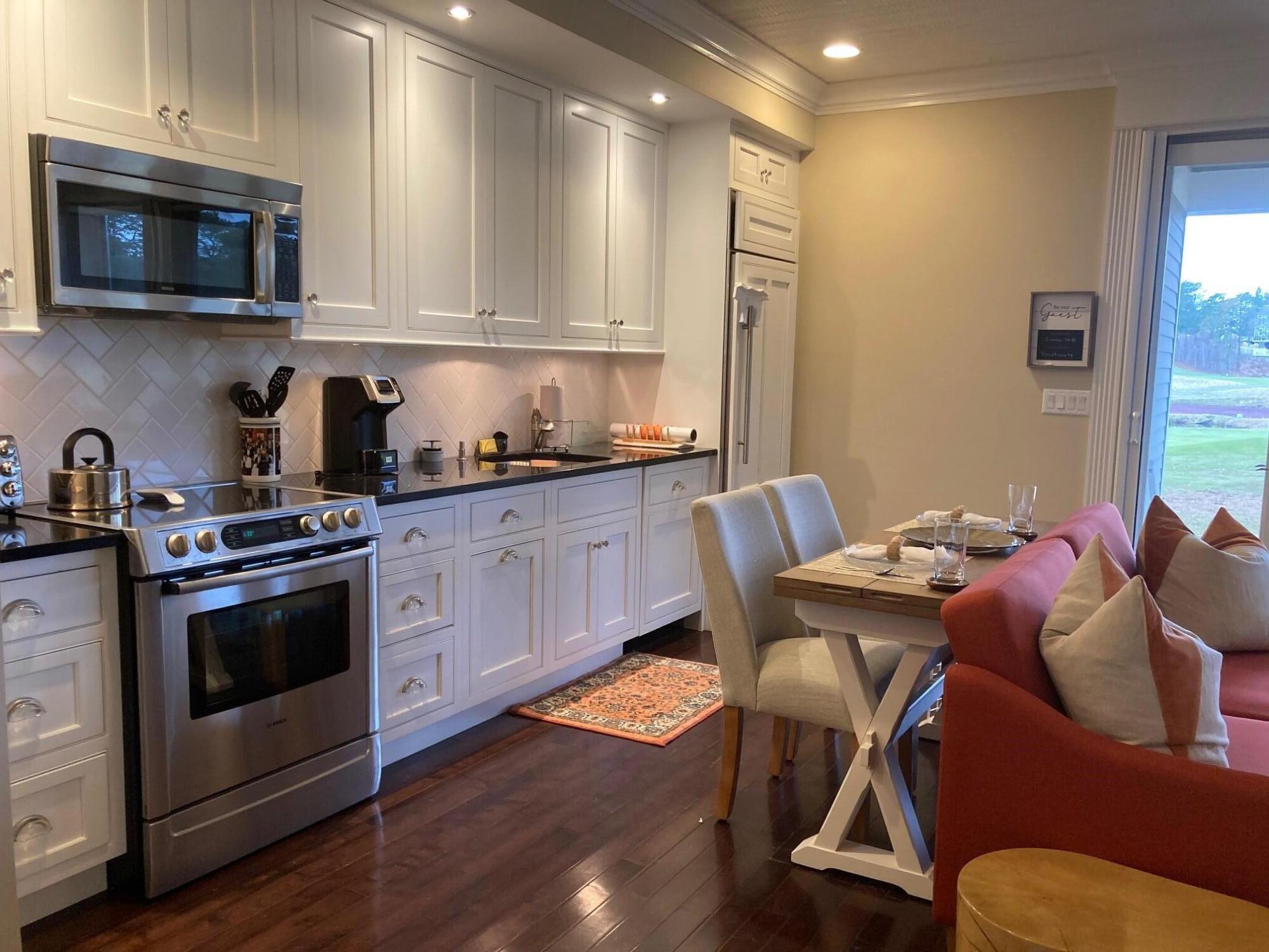 74 Simons Road, Unit B Mashpee, MA 02649 - Photo 2 of 11 a kitchen with stainless steel appliances kitchen island granite countertop a stove a sink a dining table and chairs with wooden floor