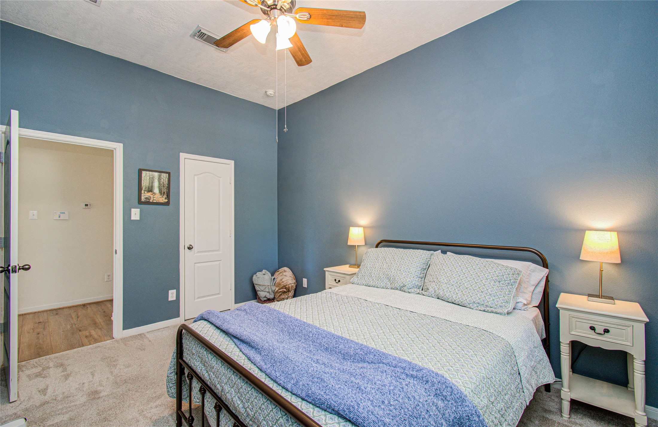 20007 Alcea Court Spring, TX 77379 - Photo 26 of 36 Cozy bedroom with blue walls and a ceiling fan, featuring a comfortable double bed, side tables with lamps, and carpeted flooring.