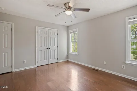 an empty room with wooden floor ceiling fan and windows