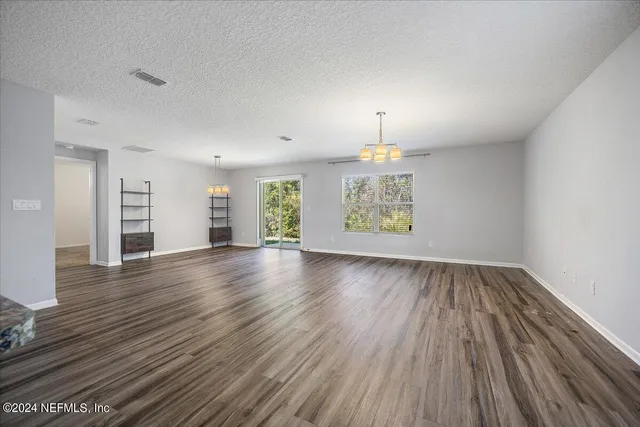 an empty room with wooden floor chandelier and windows
