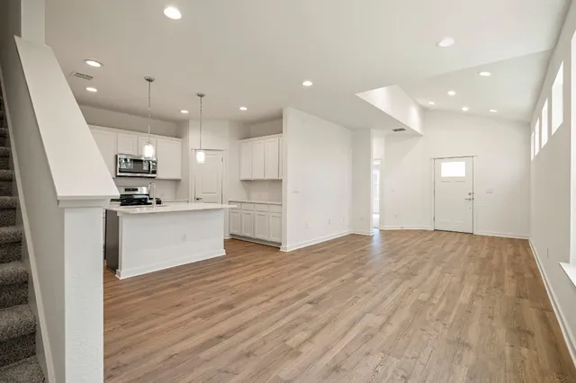 a view of kitchen with granite countertop stainless steel appliances refrigerator oven stove and white cabinets with wooden floor