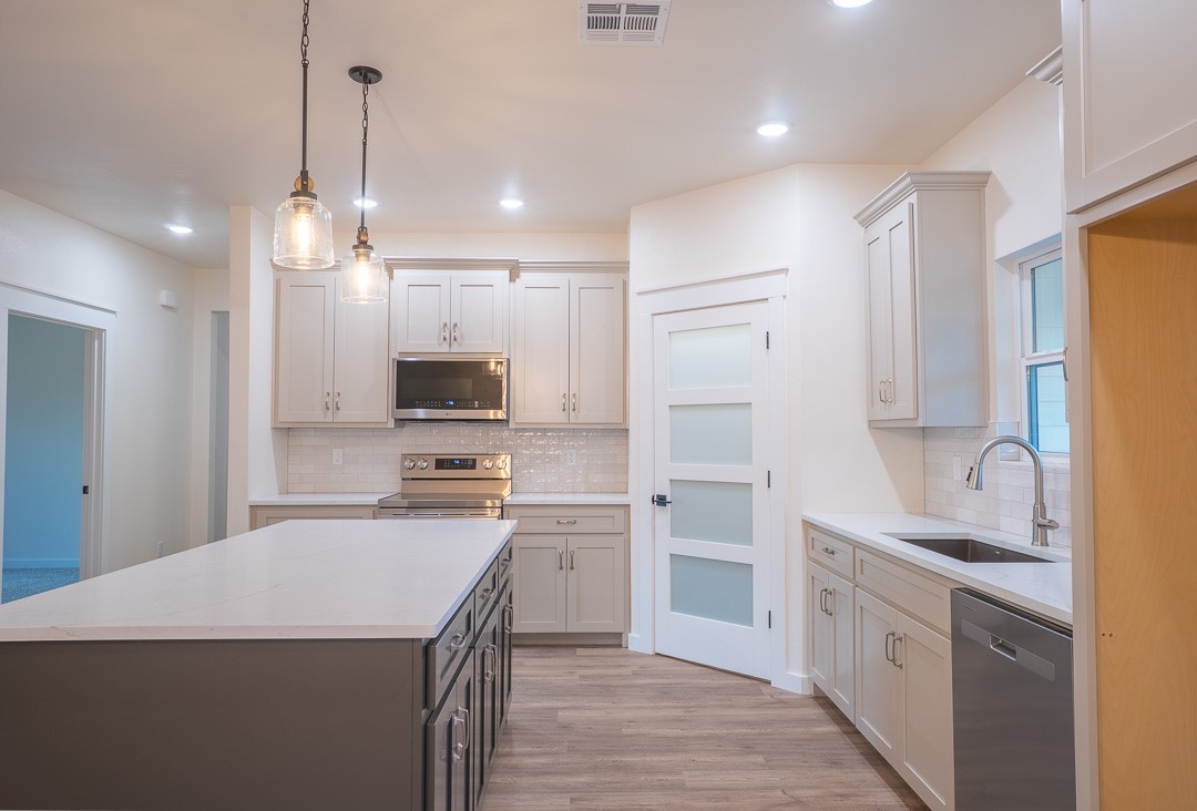 205 Blessings Way Colbert, OK 74733 - Photo 11 of 24 Kitchen featuring a large island with a light-toned countertop, wood-finish flooring, light grey cabinetry, stainless steel appliances, and pendant lighting