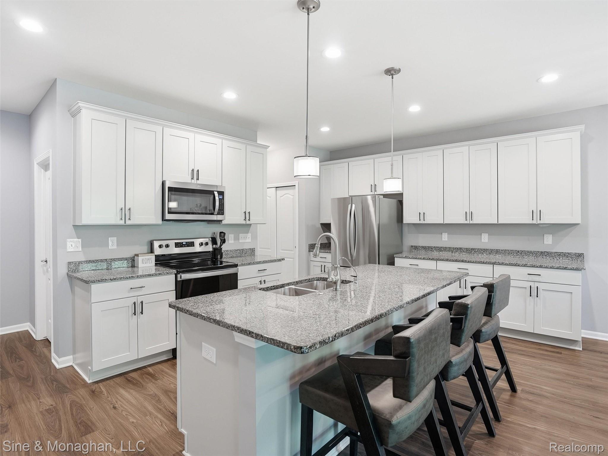 24827 Ivy Road Novi, MI 48375 - Photo 4 of 38 Modern kitchen featuring white shaker cabinetry, stainless steel appliances, a large center island with a double basin sink, recessed lighting, and wood-finish flooring