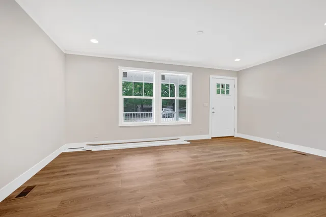 a view of an empty room with wooden floor and window