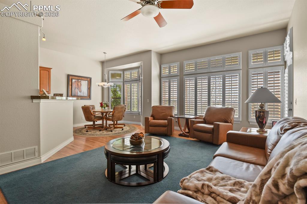 617 Concerto Drive Colorado Springs, CO 80906 - Photo 12 of 46 Bright living area featuring a ceiling fan, bay windows with plantations shutters, and hardwood flooring into the casual dining noom.