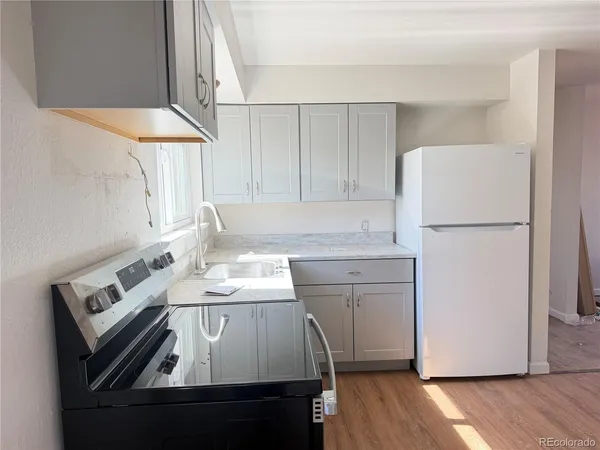 a kitchen with a sink a refrigerator a stove and white cabinets with wooden floor