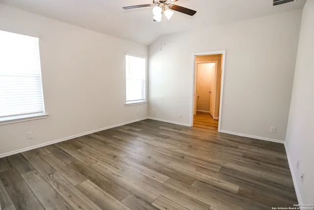 an empty room with wooden floor chandelier fan and windows