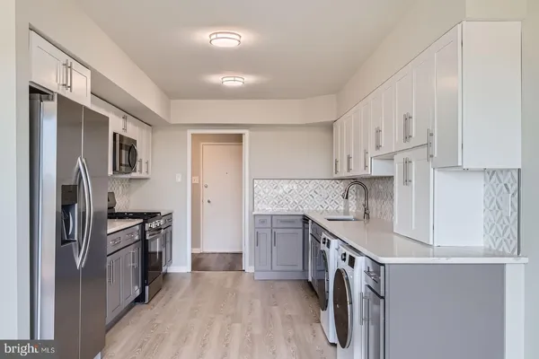 a kitchen with stainless steel appliances granite countertop a refrigerator a stove a sink and white cabinets with wooden floor