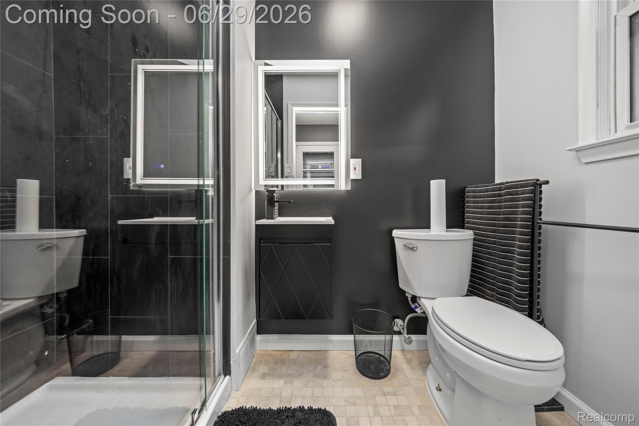 6085 Worlington Road Bloomfield Hills, MI 48301 - Photo 45 of 75 Modern bathroom featuring a glass-enclosed shower with dark tile surround, a sleek vanity with an integrated sink, an illuminated mirrored medicine cabinet, and a light-toned tile floor