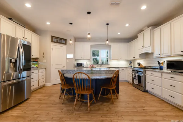 a kitchen with stainless steel appliances granite countertop a stove a refrigerator a kitchen island a table and chairs