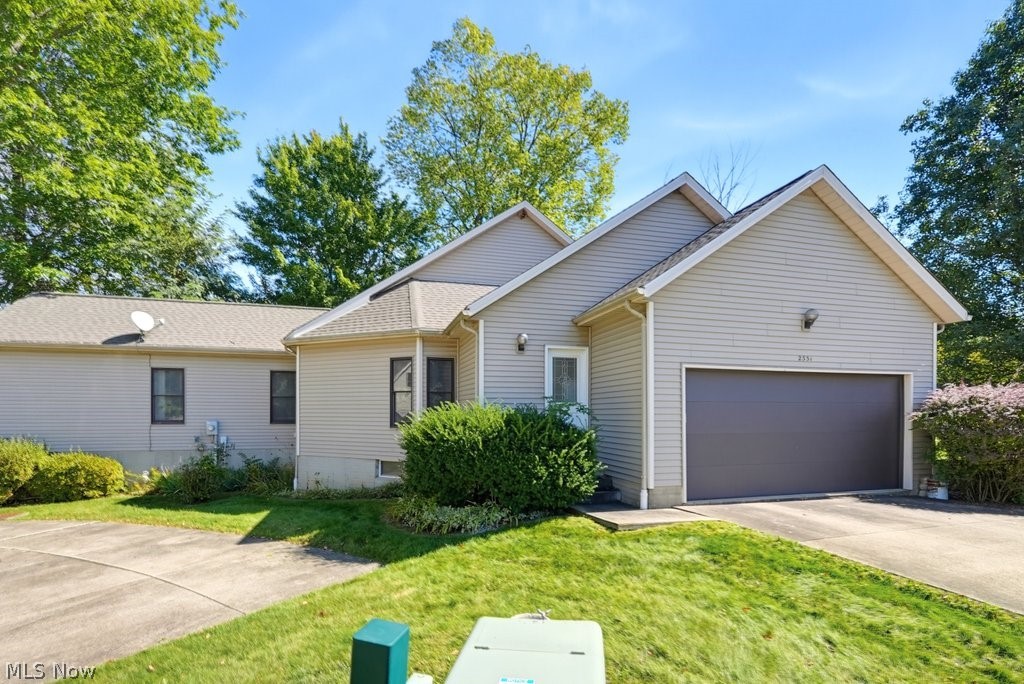 Siding exterior with an attached garage, paved driveway, mature landscaping and guest parking nearby