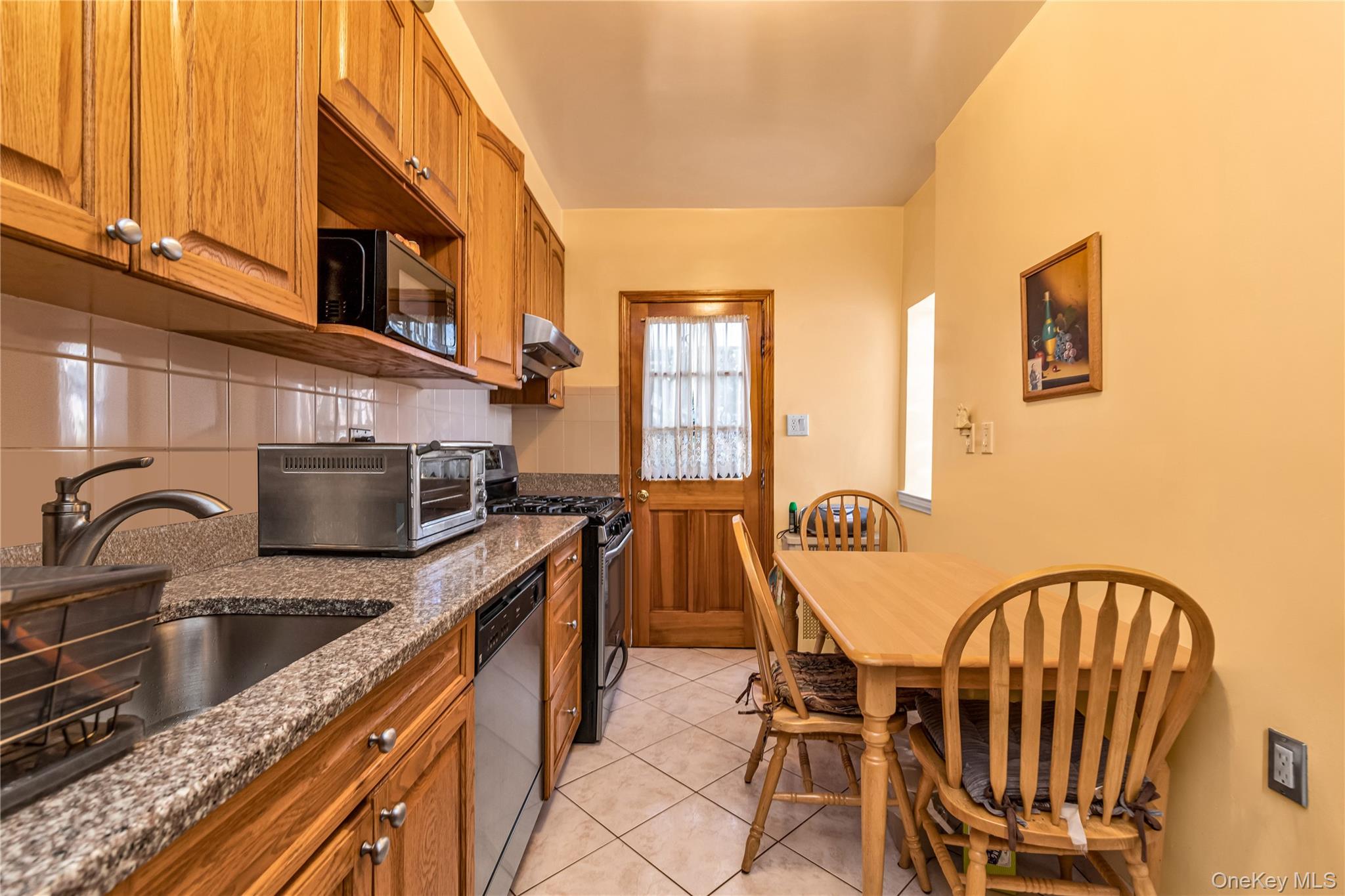 142-24 61st Road Queens, NY 11367 - Photo 6 of 18 Kitchen featuring brown cabinets, dark stone countertops, stainless steel appliances, and decorative backsplash