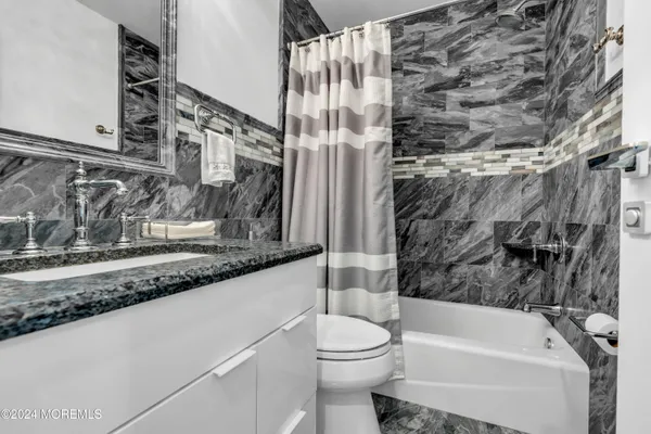 a bathroom with a granite countertop bathtub sink vanity mirror and toilet
