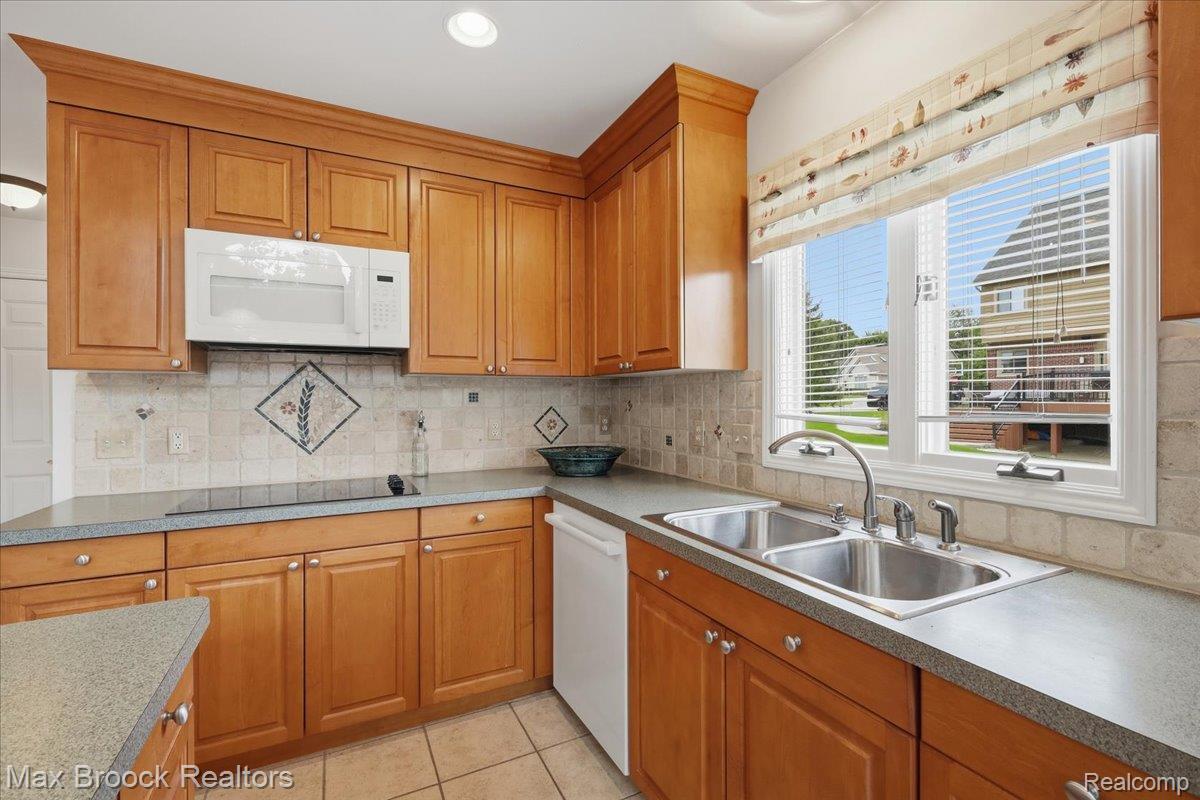 1731 Rico Road Commerce Township, MI 48382 - Photo 18 of 48 Wood-finish cabinetry, built-in microwave, tile backsplash with decorative accents, dual basin stainless steel sink, and light-toned countertops