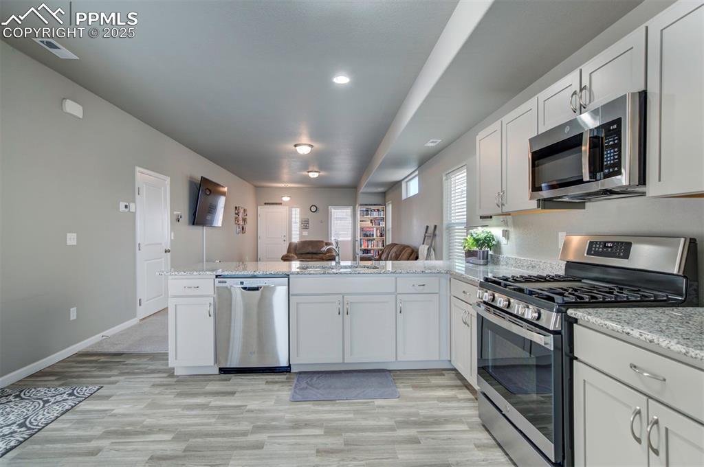 4151 Jericho Loop Colorado Springs, CO 80916 - Photo 13 of 34 a kitchen with stainless steel appliances granite countertop a stove top oven a sink dishwasher and white cabinets with wooden floor