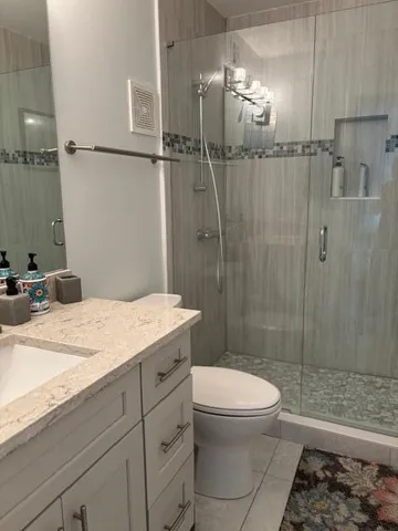 a bathroom with a granite countertop sink a toilet a mirror and shower