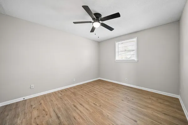 an empty room with wooden floor a ceiling fan and windows