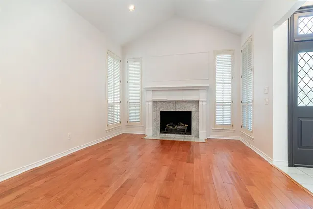 a view of an empty room with wooden floor a fireplace and a window