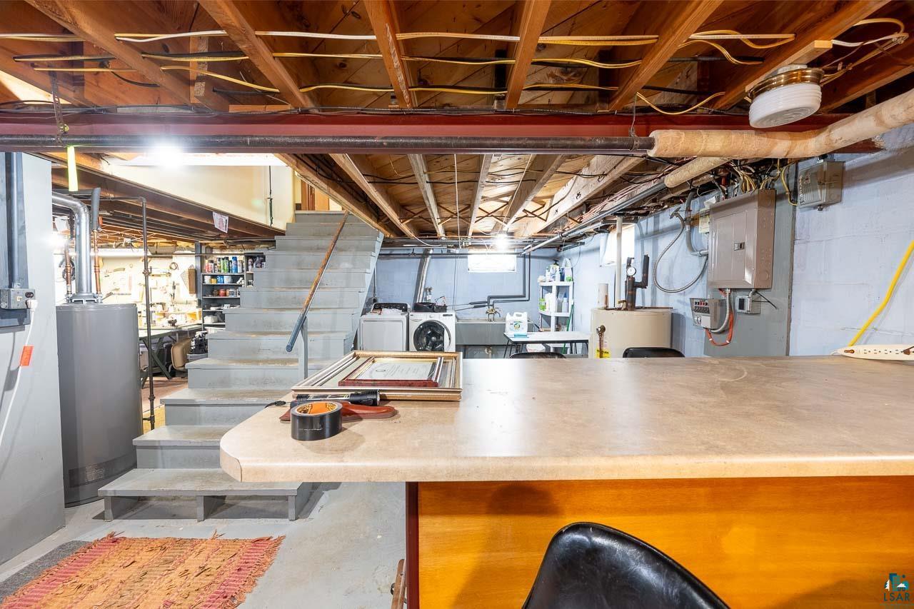 101 2nd Avenue North Biwabik, MN 55708 - Photo 26 of 44 Utility basement featuring exposed wood joists, a concrete staircase with metal railing, a laundry area with appliances, a utility sink, and a built-in countertop