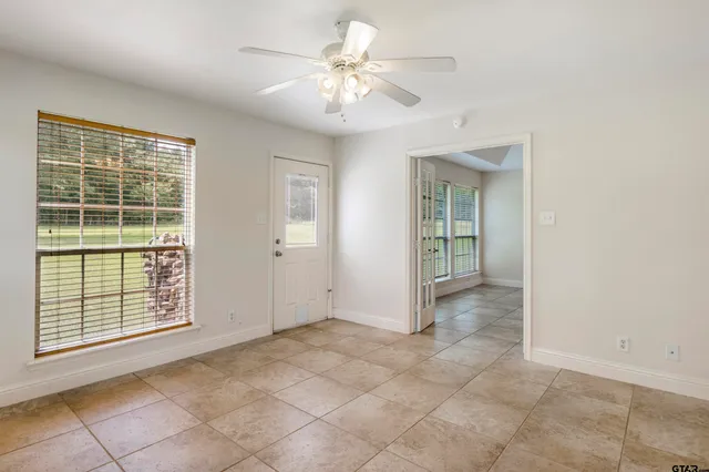 an empty room with chandelier fan and windows
