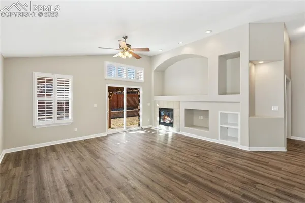 a view of an empty room with wooden floor fireplace and a window