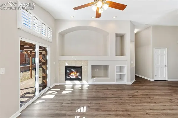 an empty room with wooden floor fire place and windows