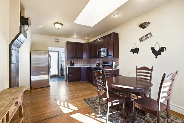 a kitchen with stainless steel appliances kitchen island granite countertop a refrigerator a stove a sink a dining table and chairs with wooden floor