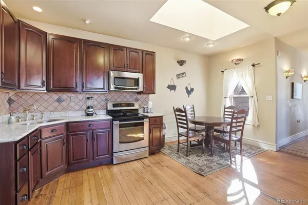 a kitchen with stainless steel appliances granite countertop a stove top oven a sink dishwasher a dining table and chairs with wooden floor