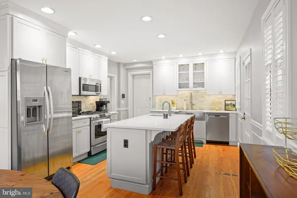 a kitchen with stainless steel appliances granite countertop a refrigerator a sink dishwasher a stove and a dining table with wooden floor