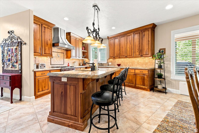 11290 South Southfield Road Mayfield, UT 84643 - Photo 53 of 103 Kitchen featuring wood cabinetry, a center island with countertop seating, tiled flooring, a stainless steel range hood, and a tiled backsplash