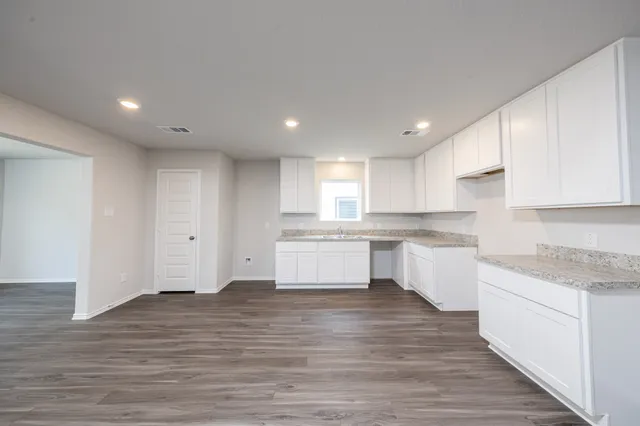 a large kitchen with stainless steel appliances granite countertop a large stove a sink and white cabinets with wooden floor