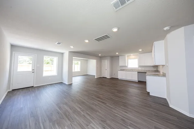 a view of an empty room with wooden floor and kitchen