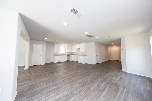 a view of an empty room with wooden floor kitchen view and a window