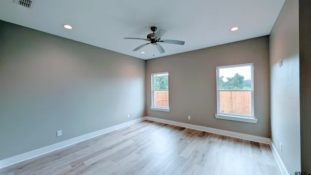an empty room with wooden floor fan and windows