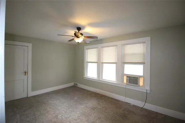 an empty room with chandelier fan and windows