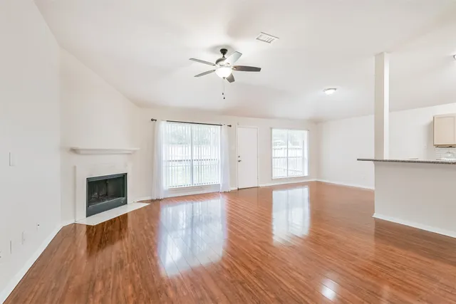 a view of an empty room with wooden floor fireplace and a window