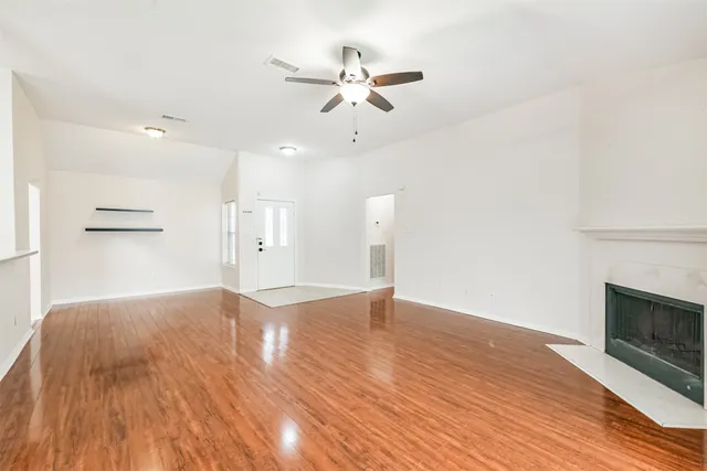 an empty room with wooden floor fan and windows