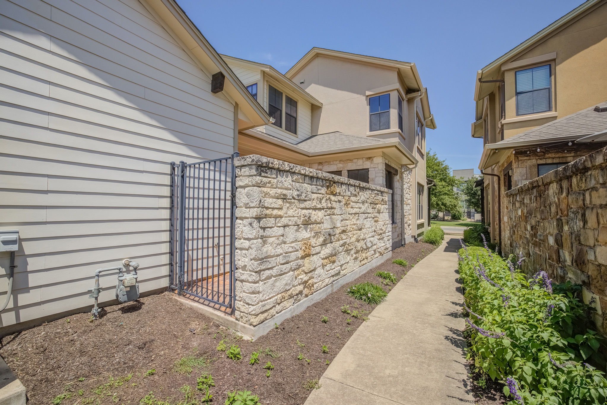 4524 Berkman Drive Austin, TX 78723 - Photo 38 of 38 Stone wall perimeter with a metal gate, featuring a concrete pathway, mature plantings, and horizontal siding